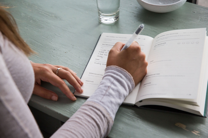 Young Woman Writing in Habit Journal on Breakfast Table
